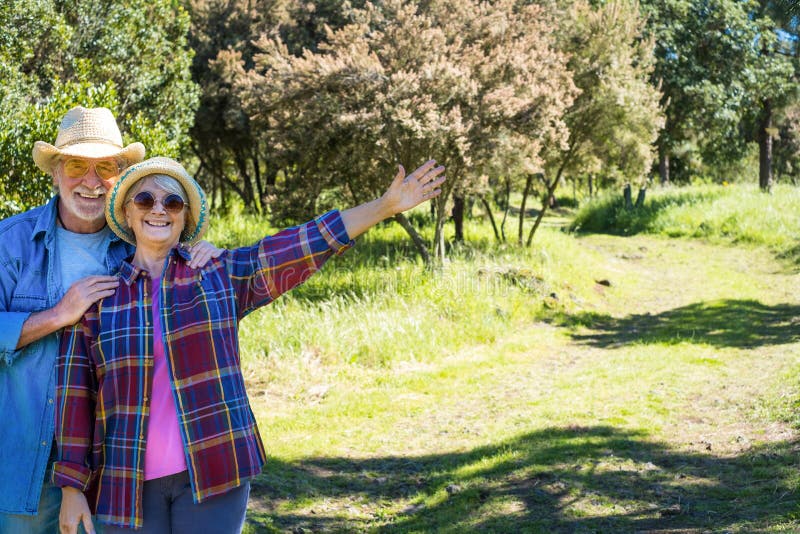 Carefree senior couple walking in the forest, green meadow and trees. Two happy retired enjoying healthy lifestyle and nature