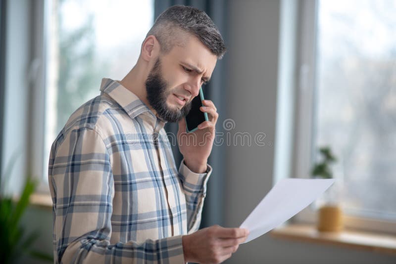 Smart young man with smartphone and sheet of paper.