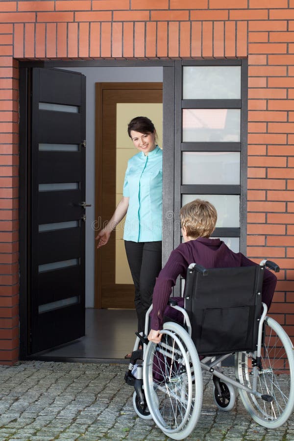 Caregiver inviting woman on wheelchair to nursing home stock photography Caregiver inviting woman on wheelchair to nursing home stock photography