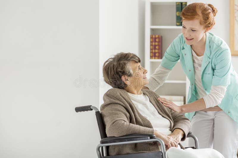 Docela mladí pečovatel pomáhá starší ženy se zdravotním postižením, v domově důchodců.