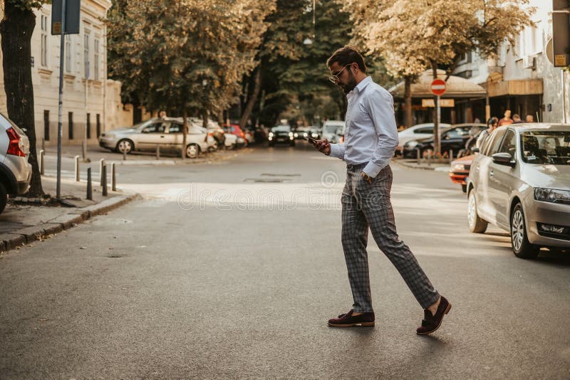 Careless handsome man with hand in his pocket looking at mobile phone while crossing the street. Careless handsome man with hand in his pocket looking at mobile phone while crossing the street