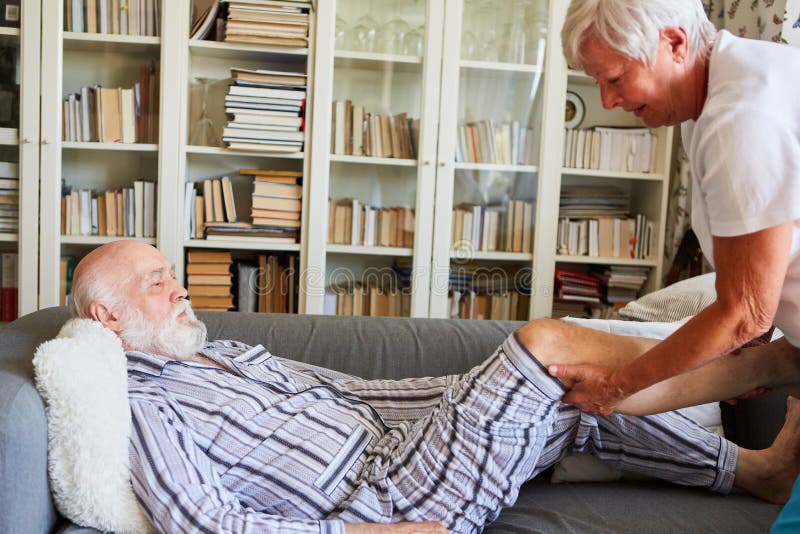 Carer treats senior knee osteoarthritis on sofa at home with physiotherapy. Carer treats senior knee osteoarthritis on sofa at home with physiotherapy