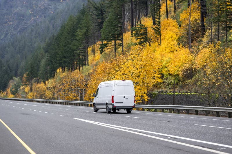 Cargo compact mini van jadący na jesiennej jesiennej drodze autostradowej z żółtymi drzewami na zboczu góry zdjęcie stock