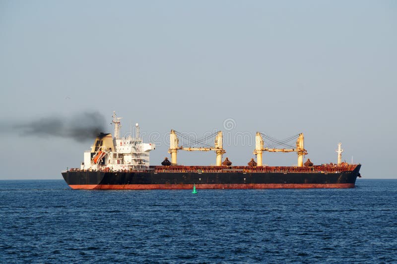 Cargo ship with black smoke from the chimney on the sea horizon