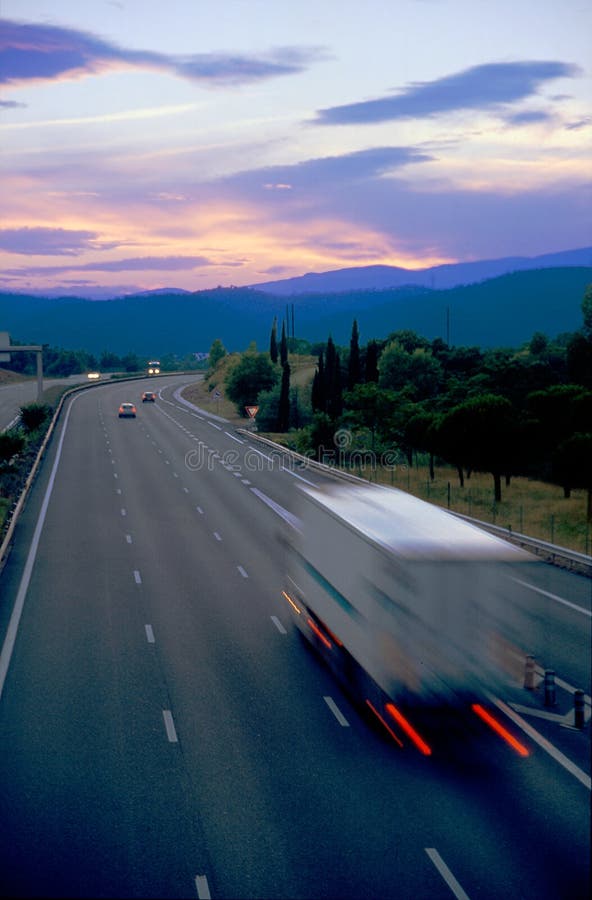 Offuscata camion carico su una strada andando verso velato montagne in un tramonto.