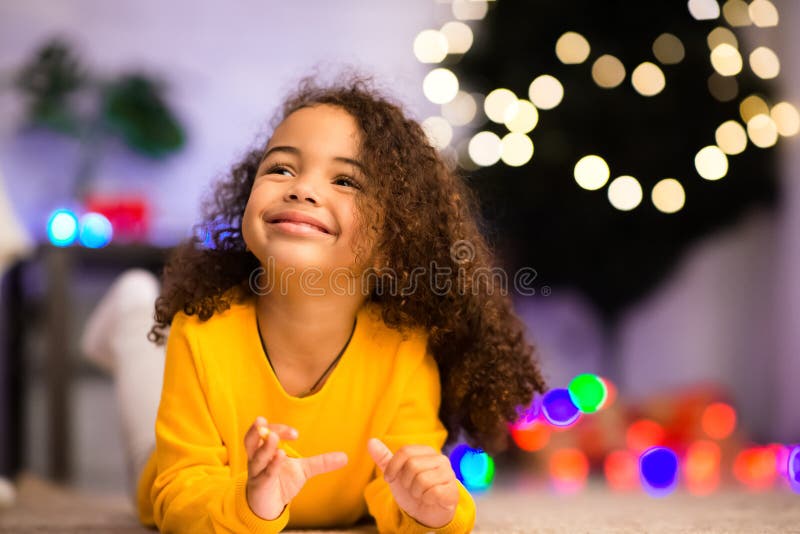 Carina bambina nera sdraiata vicino a un albero di Natale decorato fotografia stock