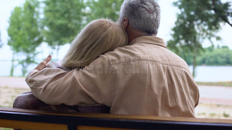 Caring aged husband covering wife with plaid blanket and hugging, tenderness