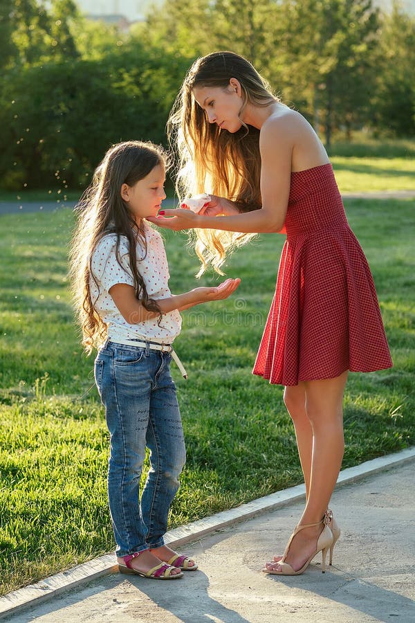 Caring and beautiful long-haired mother in cocktail red dress wipes her daughter`s face with wet napkins in the park in royalty free stock images Caring and beautiful long-haired mother in cocktail red dress wipes her daughter`s face with wet napkins in the park in royalty free stock images