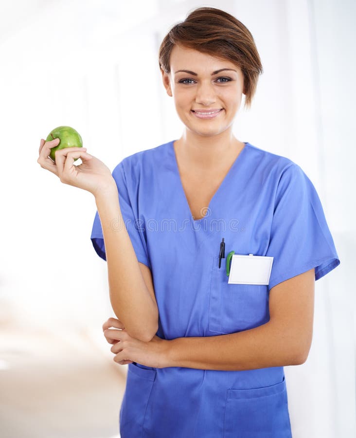Caring about her health so she can for yours. Portrait of an attractive young doctor in scrubs holding an apple. stock photography