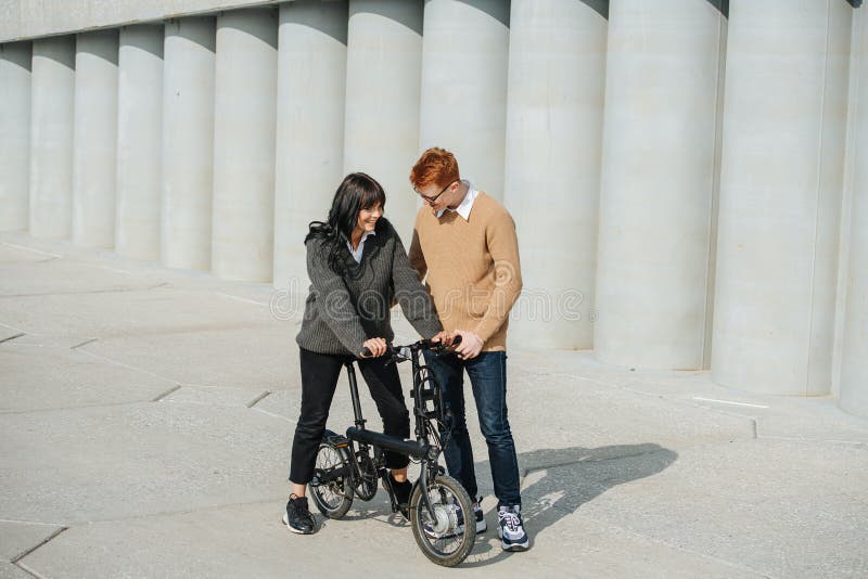 Caring man helping girlfriend ride ebike, supporting her. On a sunny autumn day