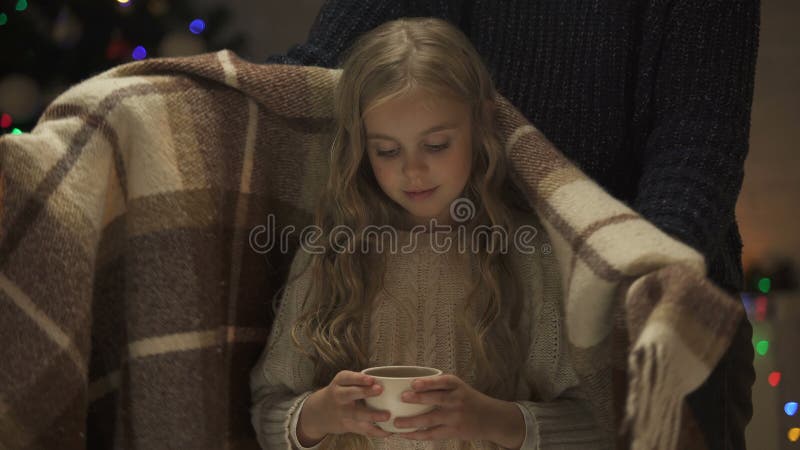 Caring mother covering cute girl holding cup of cocoa with plaid, Christmas time