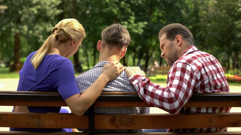 Caring mother and dad supporting sad teen son sitting on bench in park, crisis royalty free stock images Caring mother and dad supporting sad teen son sitting on bench in park, crisis royalty free stock images