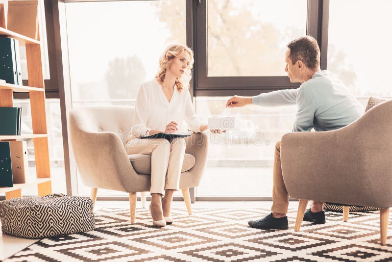 Anxious client. Caring professional psychoanalyst feeling worried while giving napkin to her anxious stressed client. Anxious client. Caring professional psychoanalyst feeling worried while giving napkin to her anxious stressed client