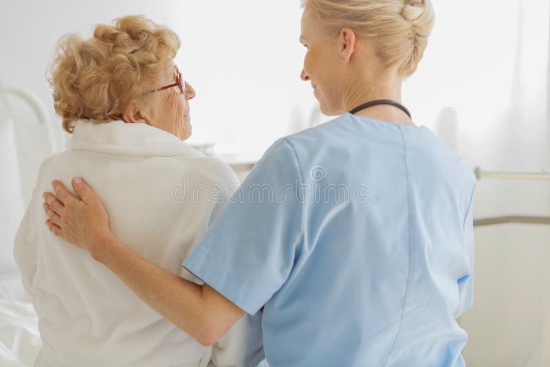 Volunteer sitting on a hospice bed next to an senior resident and strokes her back stock photo