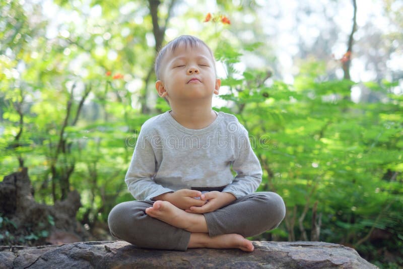 Carino bambino asiatico di 2 - 3 anni, bimbo bambino con gli occhi chiusi, a piedi nudi pratica yoga e meditazione all'aperto sul