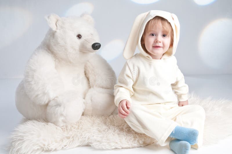 Carino bambino in costume da coniglio seduto sul pavimento con un grosso orso bianco giocattolo e felice sorriso isolato fotografie stock Carino bambino in costume da coniglio seduto sul pavimento con un grosso orso bianco giocattolo e felice sorriso isolato fotografie stock