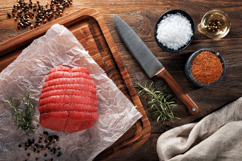 Carne asada de ternera sin hueso cruda en el papel de cocinar blanco y la tabla que corta de madera Adornado con las hierbas, las foto de archivo Carne asada de ternera sin hueso cruda en el papel de cocinar blanco y la tabla que corta de madera Adornado con las hierbas, las foto de archivo
