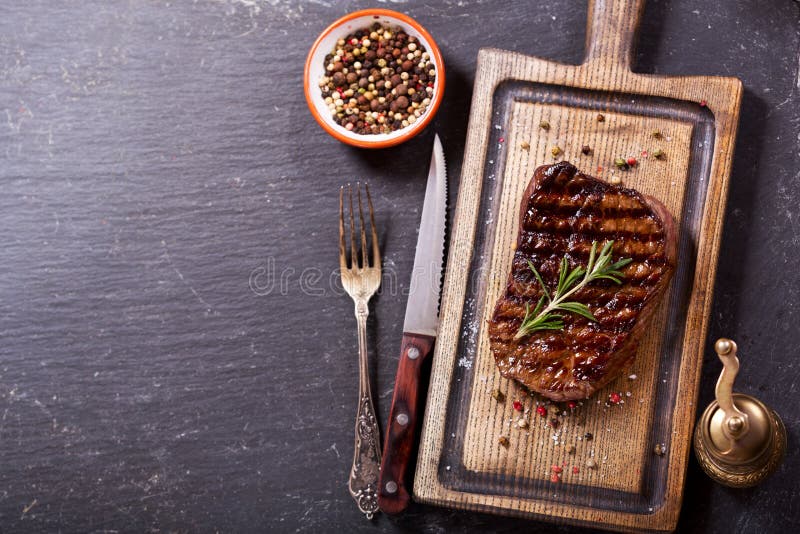 Carne asada a la parrilla con romero en el tablero de madera imagen de archivo libre de regalías Carne asada a la parrilla con romero en el tablero de madera imagen de archivo libre de regalías