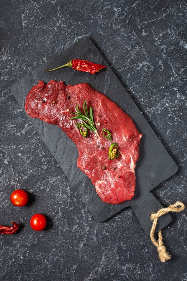Carne crua, marmoreada, bife, bife e condimentos sobre fundo de pedra escura imagem de stock royalty free Carne crua, marmoreada, bife, bife e condimentos sobre fundo de pedra escura imagem de stock royalty free