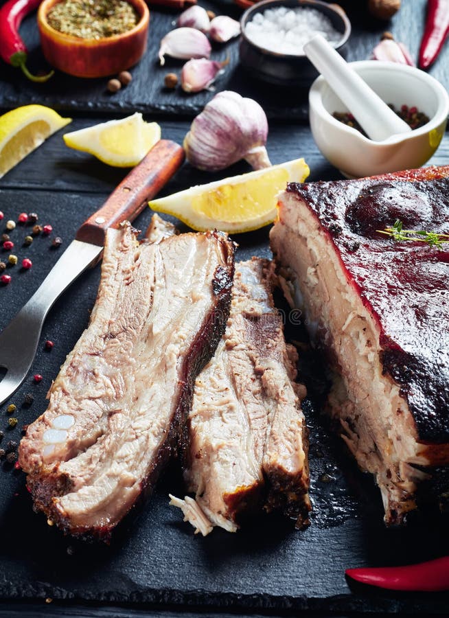 Close-up of Jamaican roasted jerk pork belly with crispy charred skin on a black slate tray with ingredients at the background, vertical view from above. Close-up of Jamaican roasted jerk pork belly with crispy charred skin on a black slate tray with ingredients at the background, vertical view from above