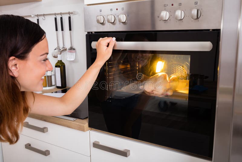 Carne di pollo di torrefazione della donna in forno fotografia stock libera da diritti Carne di pollo di torrefazione della donna in forno fotografia stock libera da diritti