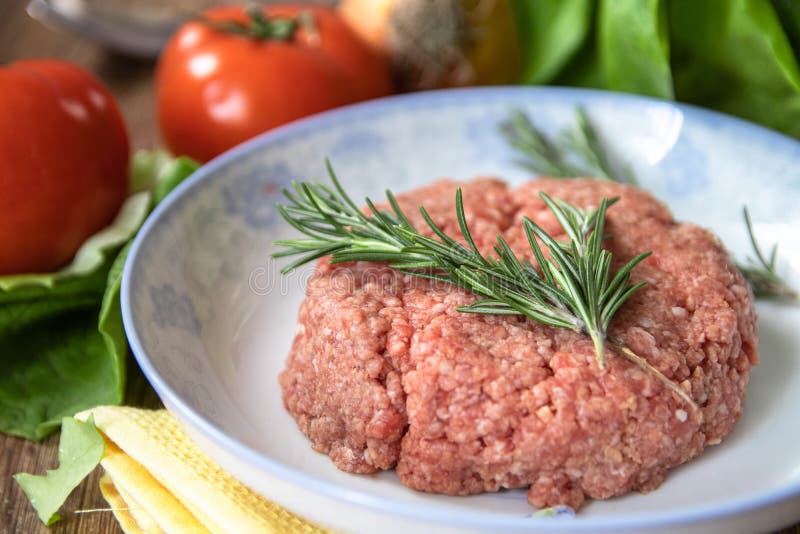 Carne picadita cruda fresca con romero en una placa y un tomate, ajo, lechuga y cebolla en la tabla de madera fotografía de archivo libre de regalías