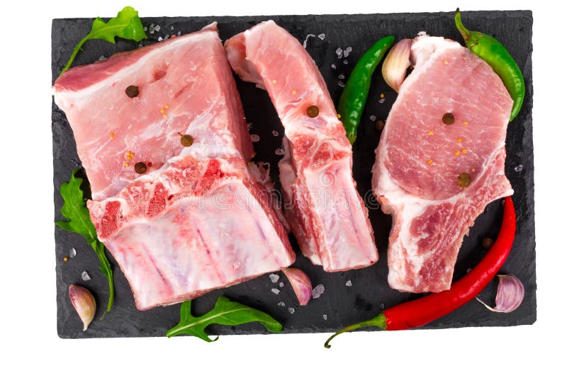 Carne suina cruda sulle ossa con peperoncino ed aglio su un'ardesia nera isolata su fondo bianco fotografia stock libera da diritti Carne suina cruda sulle ossa con peperoncino ed aglio su un'ardesia nera isolata su fondo bianco fotografia stock libera da diritti