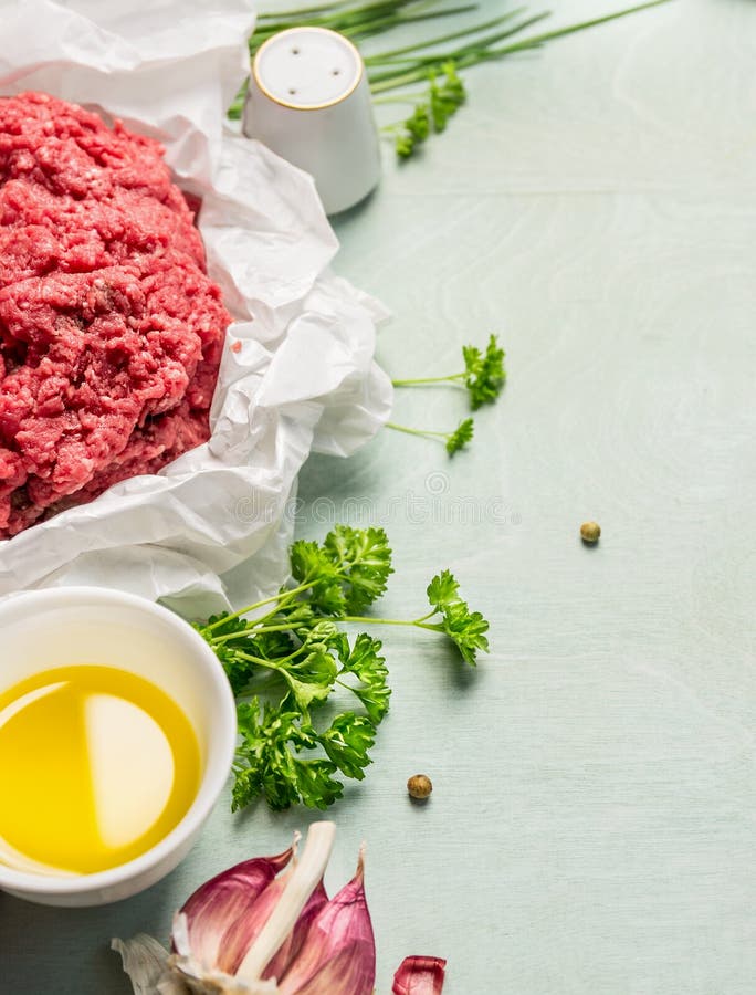 Carne tritata cruda in carta sgualcita con le erbe e l'olio freschi, preparazione su fondo di legno fotografia stock libera da diritti Carne tritata cruda in carta sgualcita con le erbe e l'olio freschi, preparazione su fondo di legno fotografia stock libera da diritti