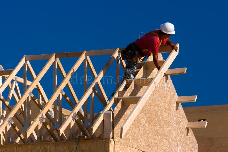 Falegname con camicia rossa e bianca hardhat la costruzione di un tetto di una casa in un cantiere edile.