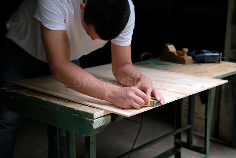 Carpenter marking straight line on plywood sheet using spirit level in carpentry workshop. Measuring, drawing line, DIY concept royalty free stock image Carpenter marking straight line on plywood sheet using spirit level in carpentry workshop. Measuring, drawing line, DIY concept royalty free stock image