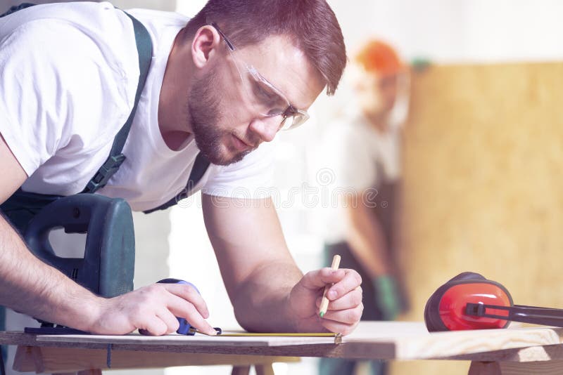 Carpenter with Pencil Drawing Project on a Piece of Wood while a Stock