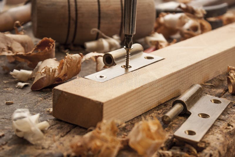 Close up of a carpenter screwed a hinge on a wooden plank