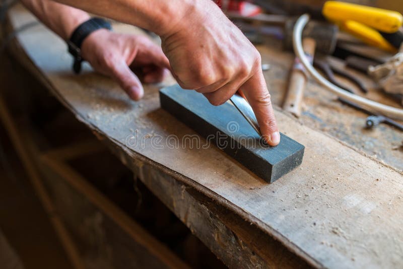 Carpenter sharpening a chisel in a small workshop, focus on the index finger.