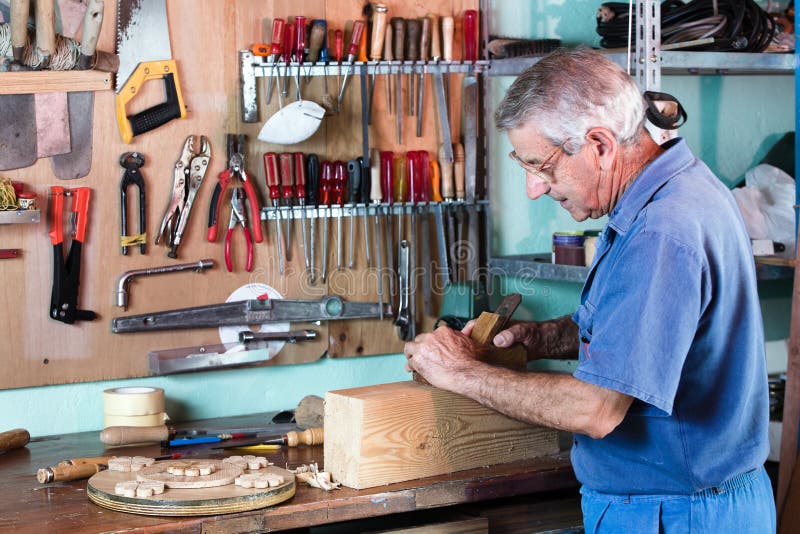 Cabinetmaker sanding a piece of wood in his workshop with tools on the background. carpenter working with wood