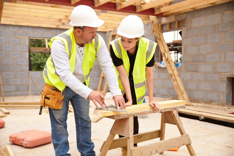 Carpentiere With Female Apprentice che lavora al cantiere fotografia stock libera da diritti Carpentiere With Female Apprentice che lavora al cantiere fotografia stock libera da diritti