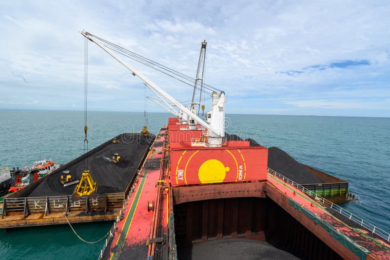 Carregamento de carvão proveniente de barcos de carga num navio a granel utilizando guindastes de navio. imagem de stock Carregamento de carvão proveniente de barcos de carga num navio a granel utilizando guindastes de navio. imagem de stock