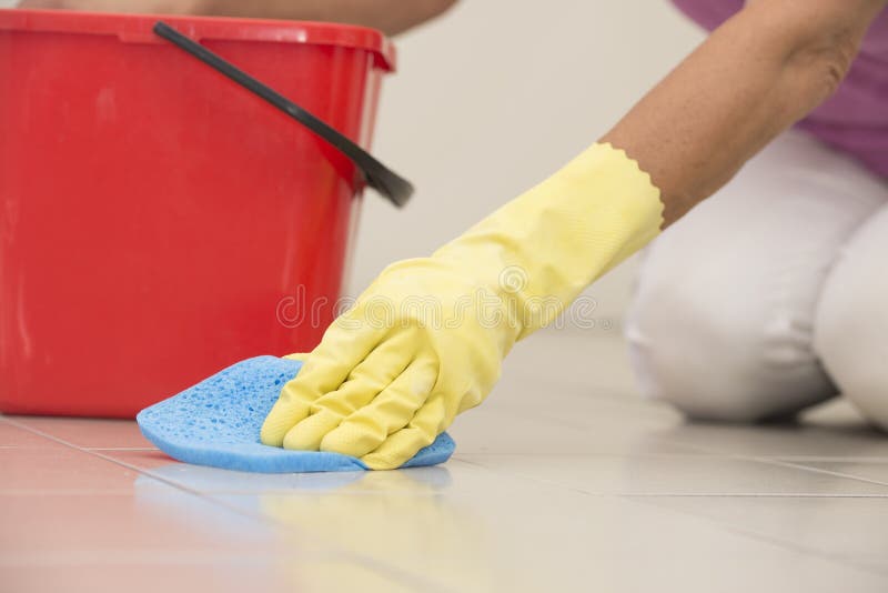 Close up Hand in yellow rubber glove cleaning floor tiles with sponge, with woman, housewife in blurred background and copy space. Close up Hand in yellow rubber glove cleaning floor tiles with sponge, with woman, housewife in blurred background and copy space.