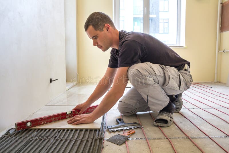 Carreleur de jeune travailleur installant les carreaux de c?ramique utilisant le levier sur le plancher de ciment avec le syst?me photo libre de droits Carreleur de jeune travailleur installant les carreaux de c?ramique utilisant le levier sur le plancher de ciment avec le syst?me photo libre de droits