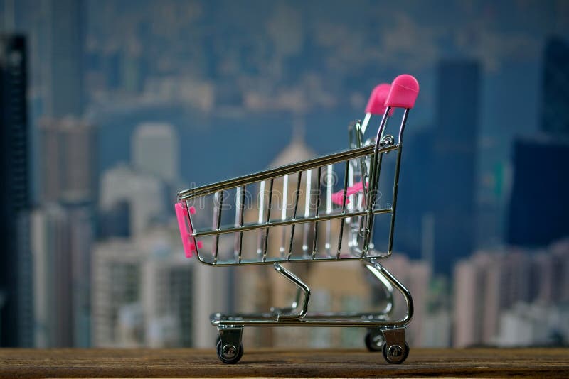 Carrello o carrello del supermercato sulla tavola di lavoro di legno superiore con il fondo dell'edificio per uffici della città fotografia stock libera da diritti Carrello o carrello del supermercato sulla tavola di lavoro di legno superiore con il fondo dell'edificio per uffici della città fotografia stock libera da diritti