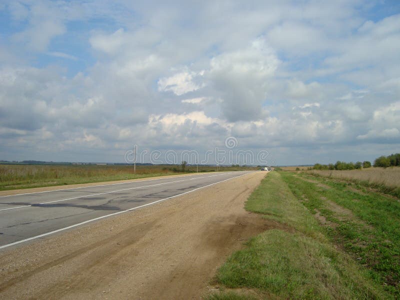 Carretera de asfalto directa a través del campo debajo del cielo, en el cual las nubes flotan fotos de archivo libres de regalías Carretera de asfalto directa a través del campo debajo del cielo, en el cual las nubes flotan fotos de archivo libres de regalías