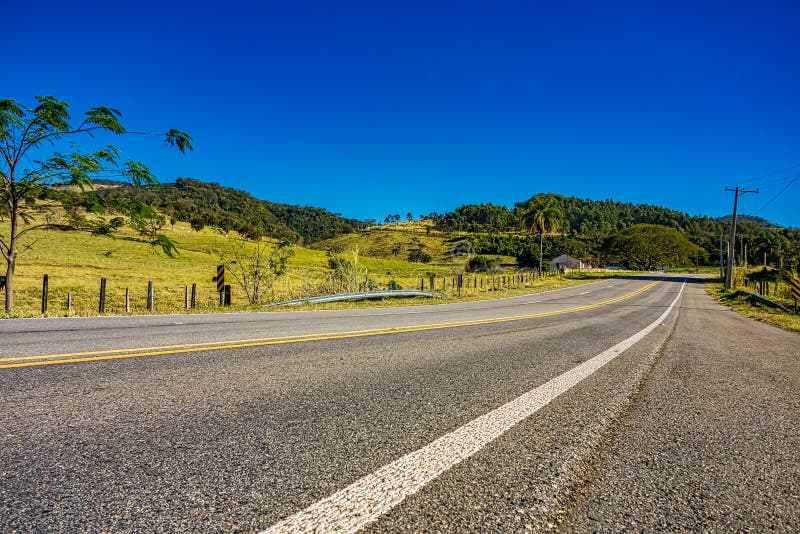 Carretera entre las colinas en Minas Gerais, el Brasil, con el cielo azul y el pasto con ganado por otra parte foto de archivo Carretera entre las colinas en Minas Gerais, el Brasil, con el cielo azul y el pasto con ganado por otra parte foto de archivo