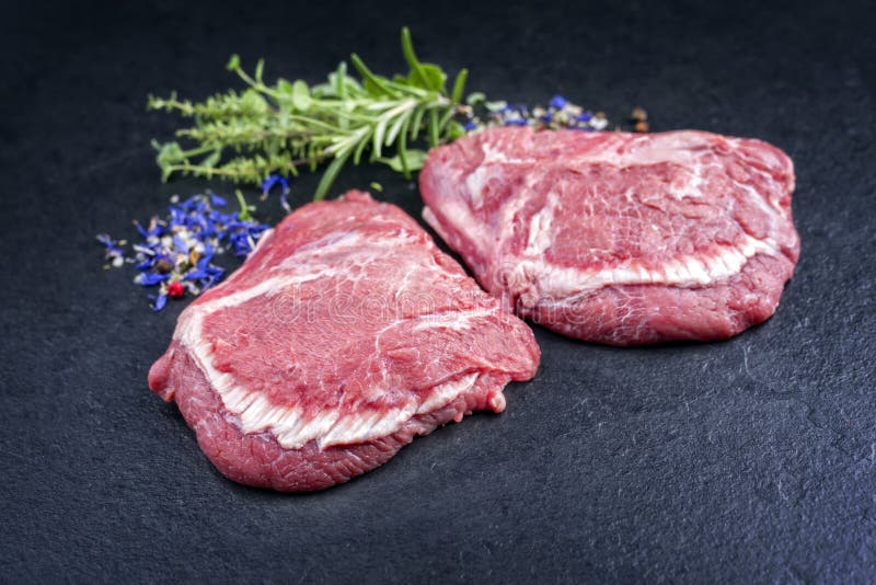 Traditional German raw beef cheeks offered as closeup on a black board with copy space. Traditional German raw beef cheeks offered as closeup on a black board with copy space