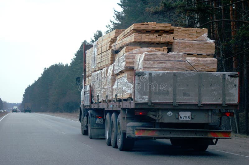 Truck with sawn timber cargo in motion on public road at dark spring day. Truck with sawn timber cargo in motion on public road at dark spring day