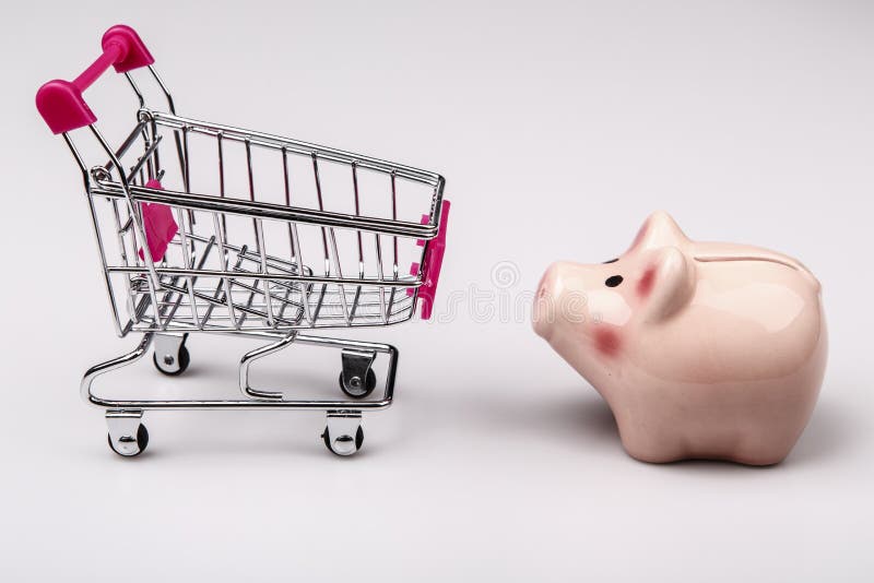 Carro de la compra contra la caja de dinero del cerdo fotos de archivo libres de regalías