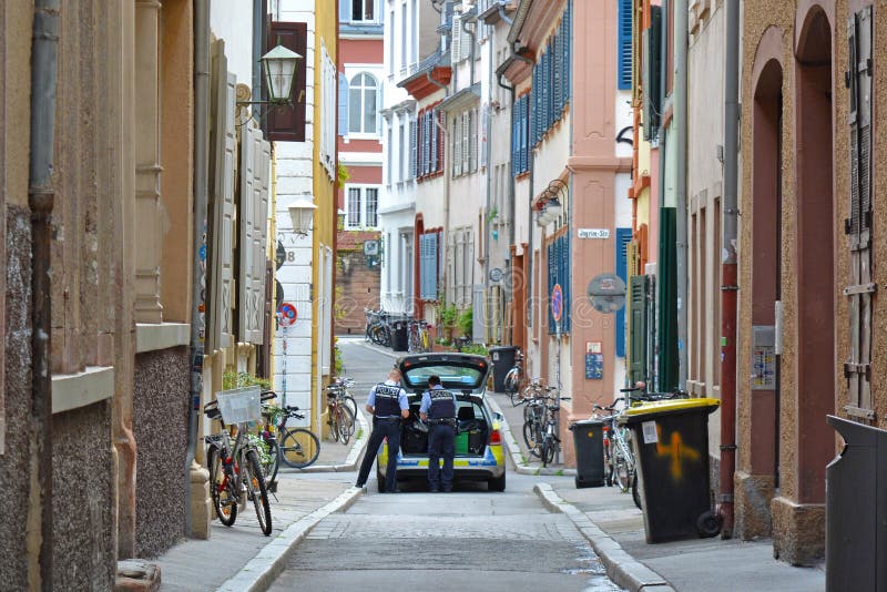 Carro de polícia com os dois oficiais na patrulha na rua secundária do centro da cidade histórico imagem de stock Carro de polícia com os dois oficiais na patrulha na rua secundária do centro da cidade histórico imagem de stock