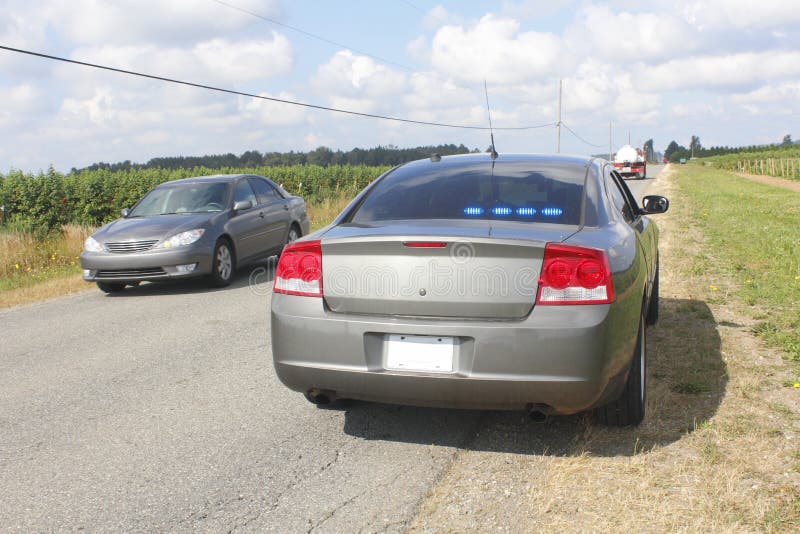 An unmarked police cruiser is parked on the side of a road while vehicles carefully pass by. An unmarked police cruiser is parked on the side of a road while vehicles carefully pass by.