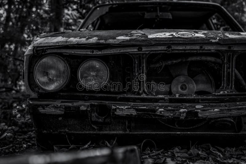 Carro destruído velho na cena preto e branco Carro oxidado abandonado na opinião dianteira do close up da floresta do carro destr fotografia de stock royalty free Carro destruído velho na cena preto e branco Carro oxidado abandonado na opinião dianteira do close up da floresta do carro destr fotografia de stock royalty free