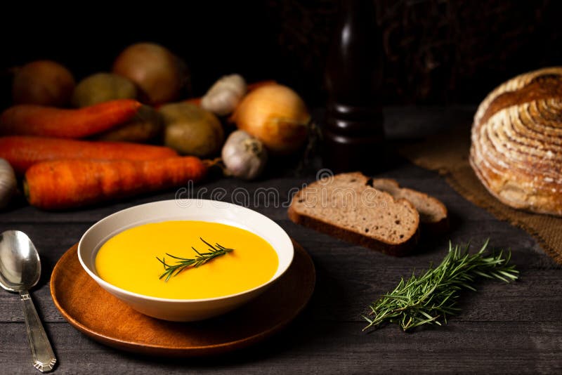 Carrot and potato soup with rosemary twig on a grey wood table, alongside a vintage silver spoon, onions, potatoes, carrots, bread royalty free stock images Carrot and potato soup with rosemary twig on a grey wood table, alongside a vintage silver spoon, onions, potatoes, carrots, bread royalty free stock images
