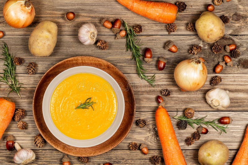 Carrot and potato soup bowl on drift wood table with a spread of vegetables, acorns, pine cones, garlic, and rosemary. Flat lay royalty free stock image Carrot and potato soup bowl on drift wood table with a spread of vegetables, acorns, pine cones, garlic, and rosemary. Flat lay royalty free stock image