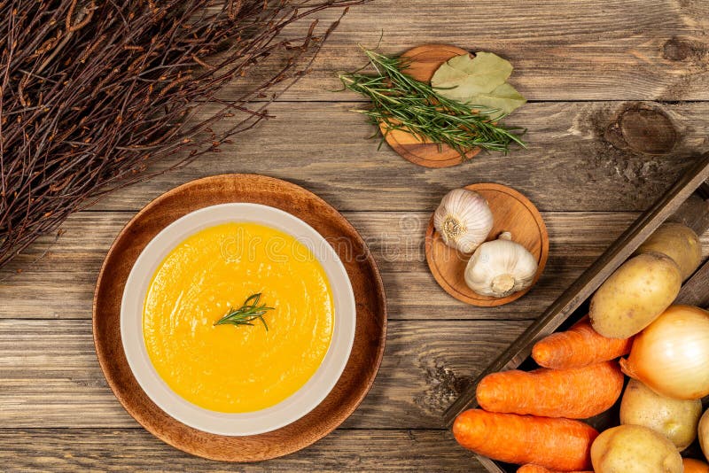 Carrot and potato soup bowl on a drift wood table with vegetables in a crate, dry wood branches, garlic, laurel and rosemary. royalty free stock photo Carrot and potato soup bowl on a drift wood table with vegetables in a crate, dry wood branches, garlic, laurel and rosemary. royalty free stock photo